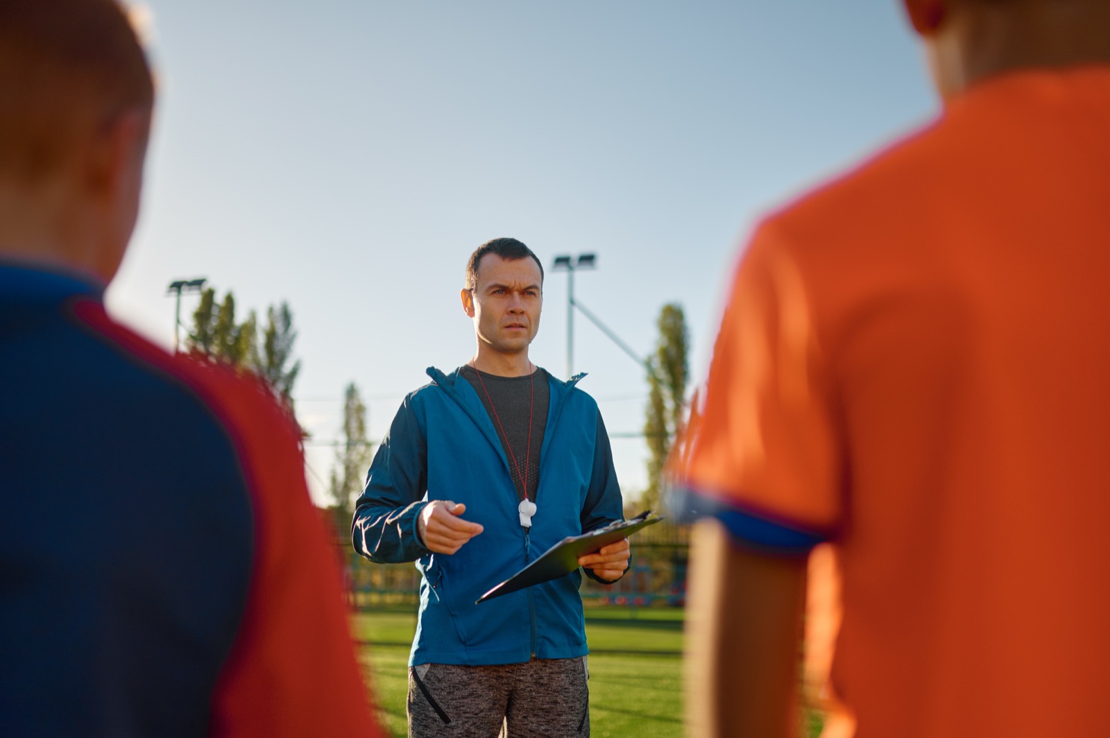 Coach addressing his team of teenage athletes with a clipboard on the field